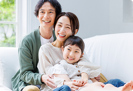 両親と子供が互いに顔を寄せ合いながら並んでソファーに座っている写真