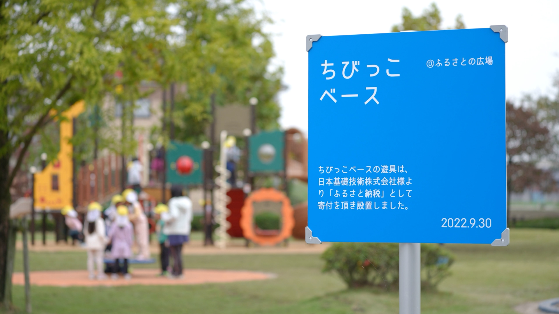 ちびっこベースの青い立て札の後ろにジャングルジムのような遊具が写っている様子