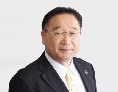 明和町の冨塚町長が、紺色のスーツを着て微笑んでいる