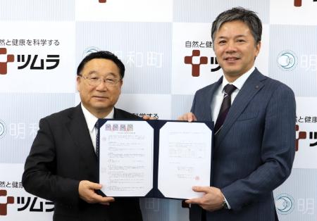 株式会社ツムラの杉井COOと冨塚町長が協定書をもって微笑んでいる